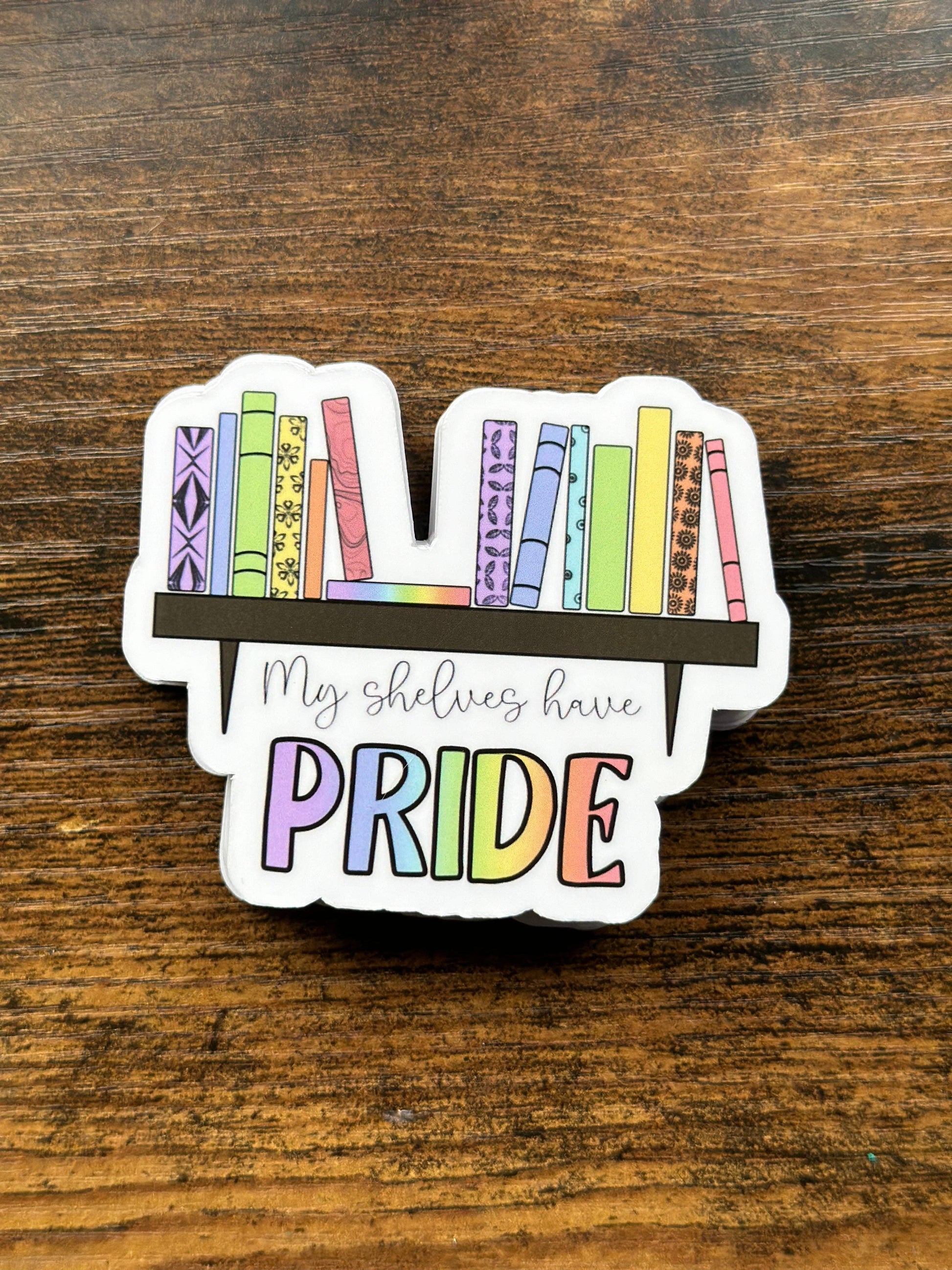 Sticker with rainbow books and 'My shelves have PRIDE' text on a wooden surface