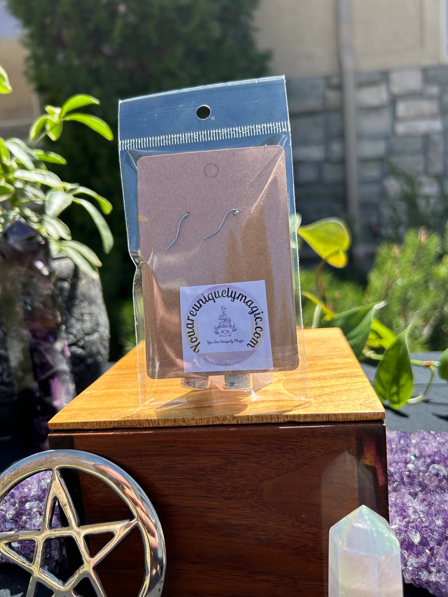 Packaged earrings on a wooden stand with a blurred outdoor background