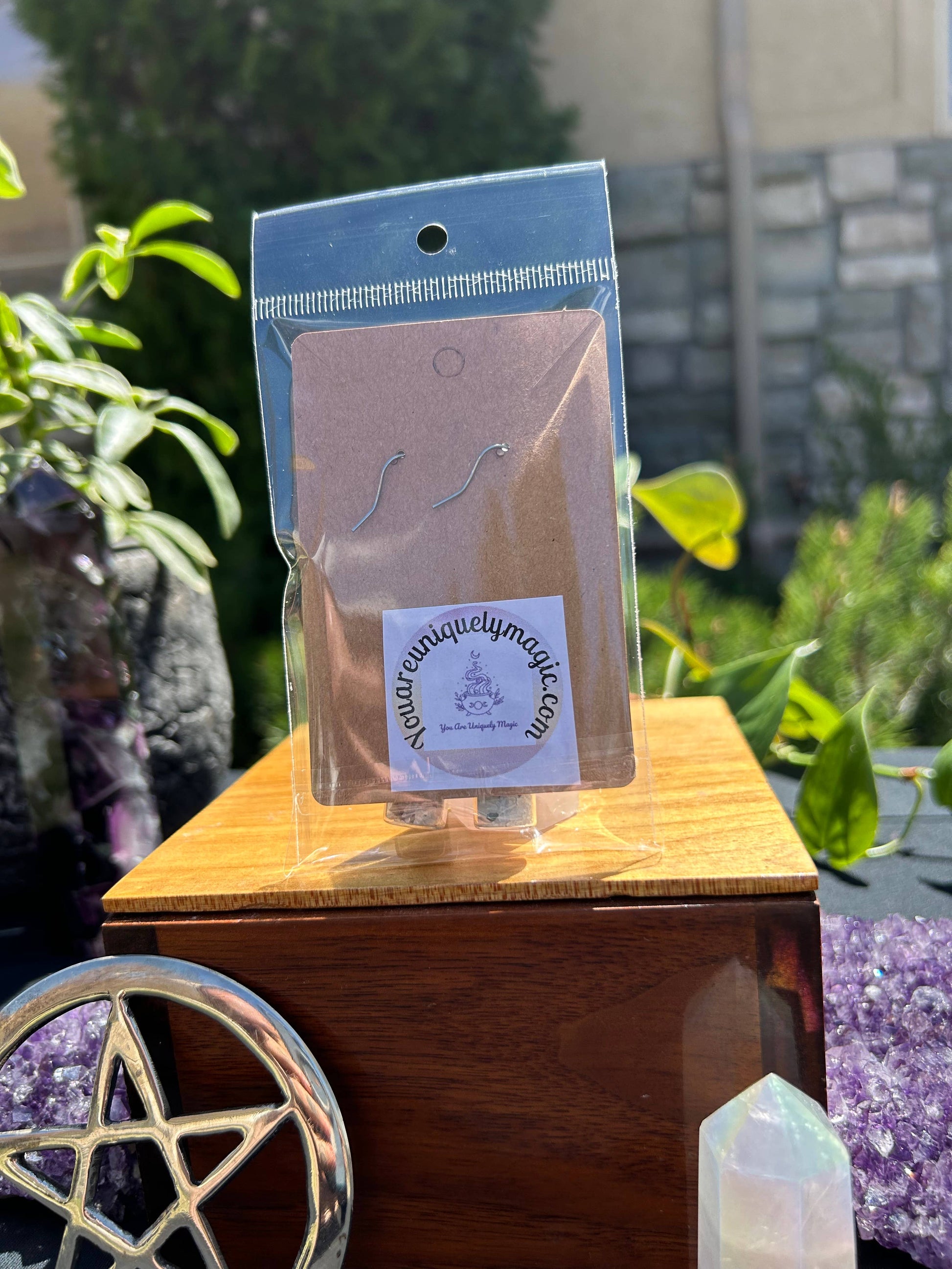 Packaged earrings on a wooden stand with a blurred outdoor background