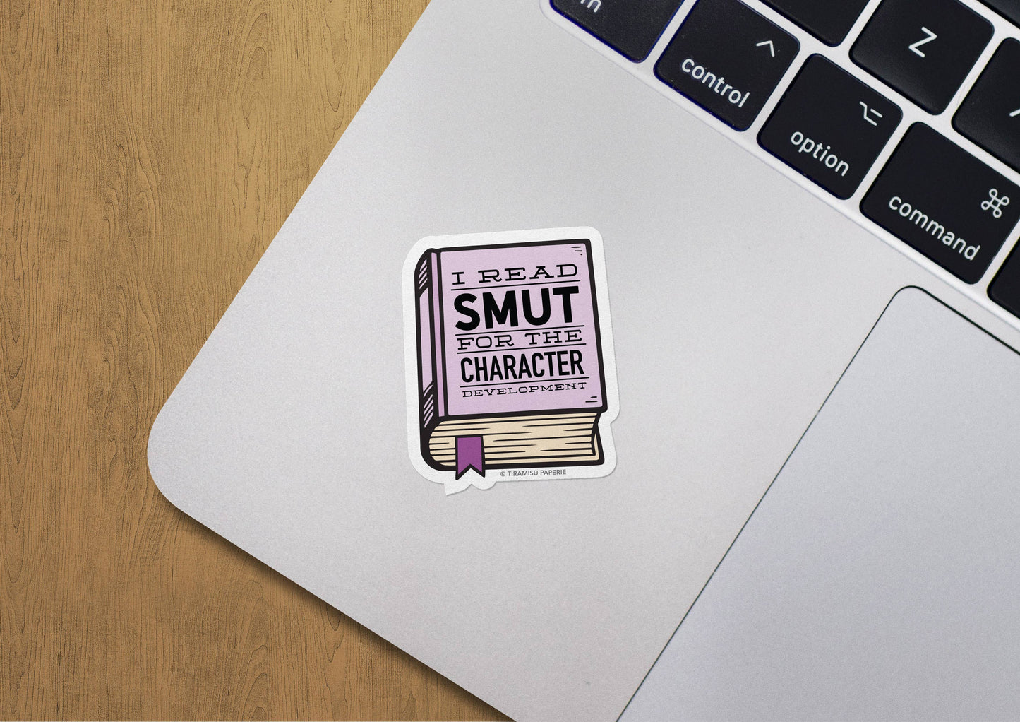 Laptop with a sticker reading 'I Read SMUT for Character Development' on a wooden surface