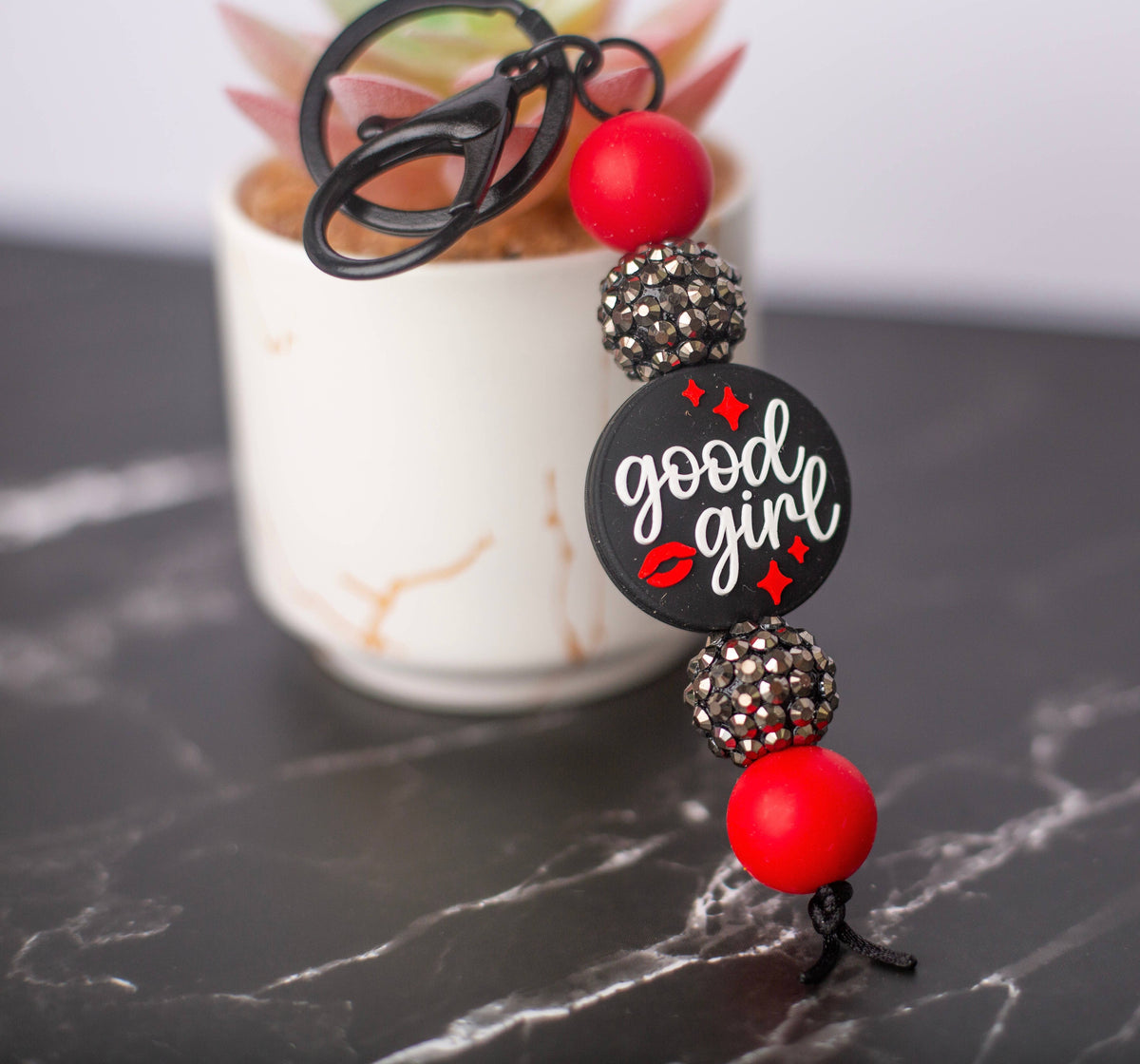 Keychain with 'good girl' text and red beads on a marble surface