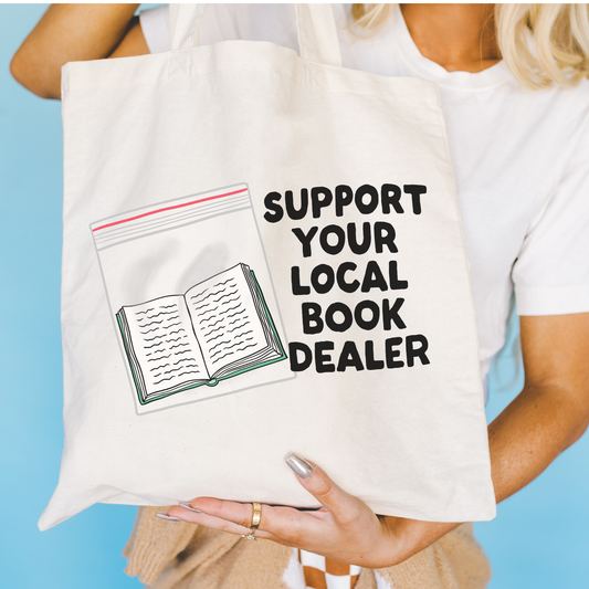 Person holding a tote bag with 'Support Your Local Book Dealer' text and a book illustration.