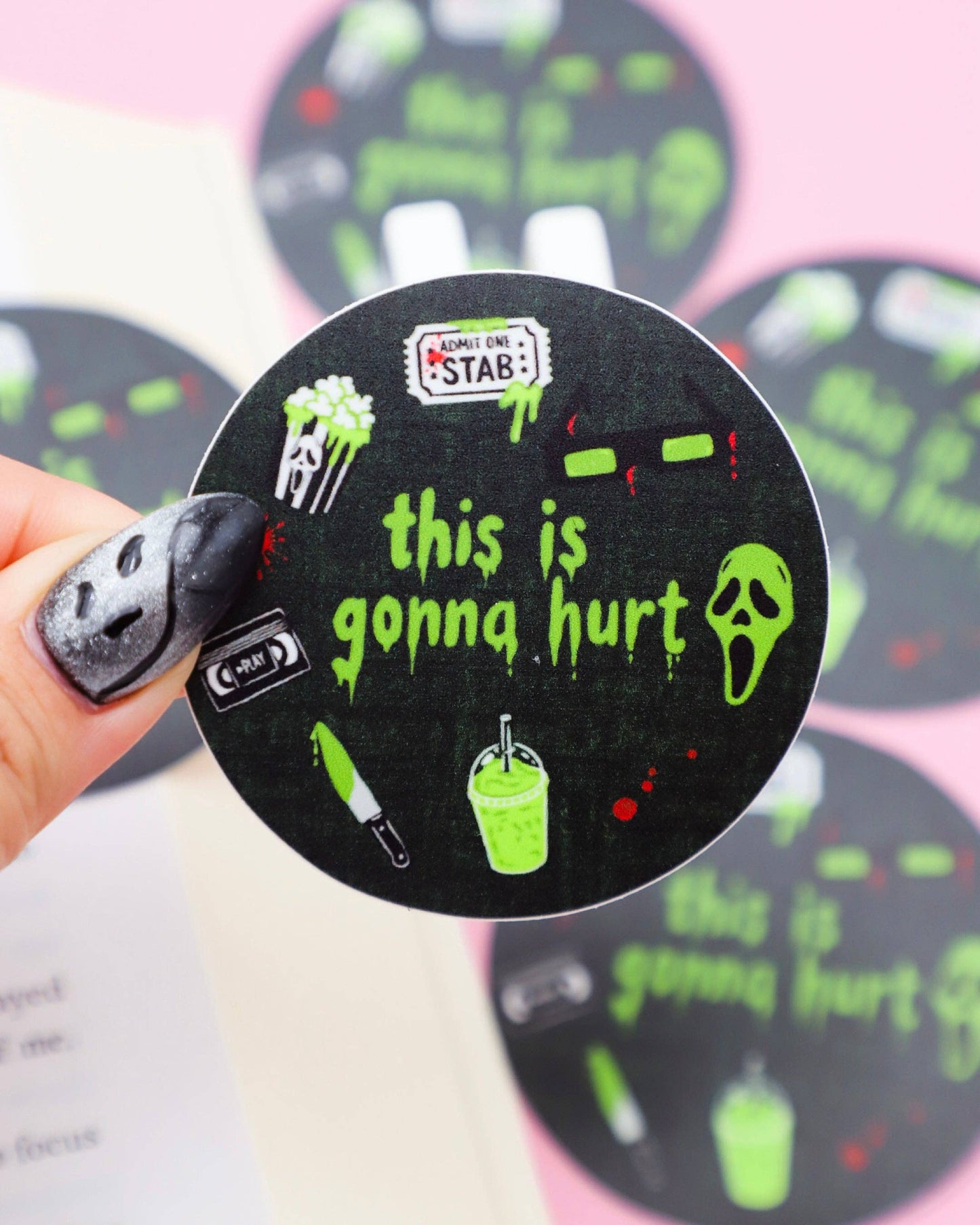 Circular sticker with text 'this is gonna hurt' held by a hand against a pink background