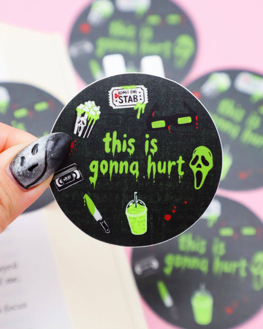 Circular sticker with text 'this is gonna hurt' held by a hand against a pink background
