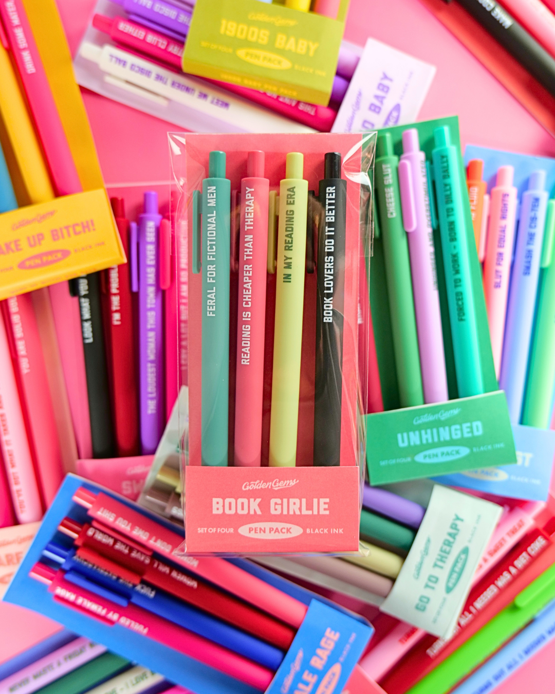 Assorted colorful pens and markers with visible text on a pink background