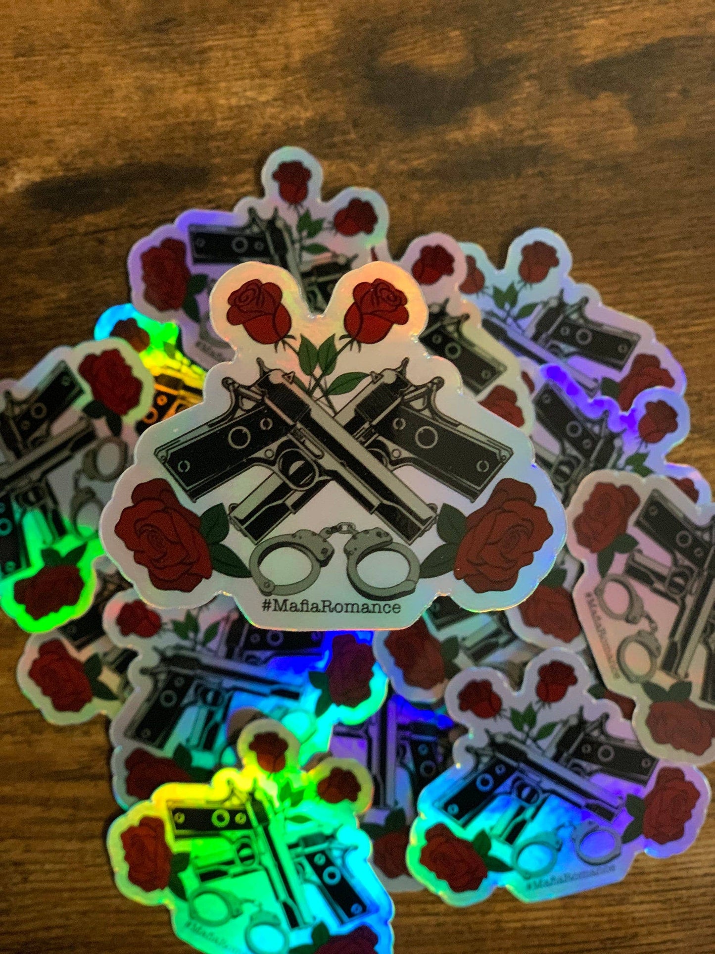 Holographic stickers with roses, guns, and handcuffs on a wooden surface