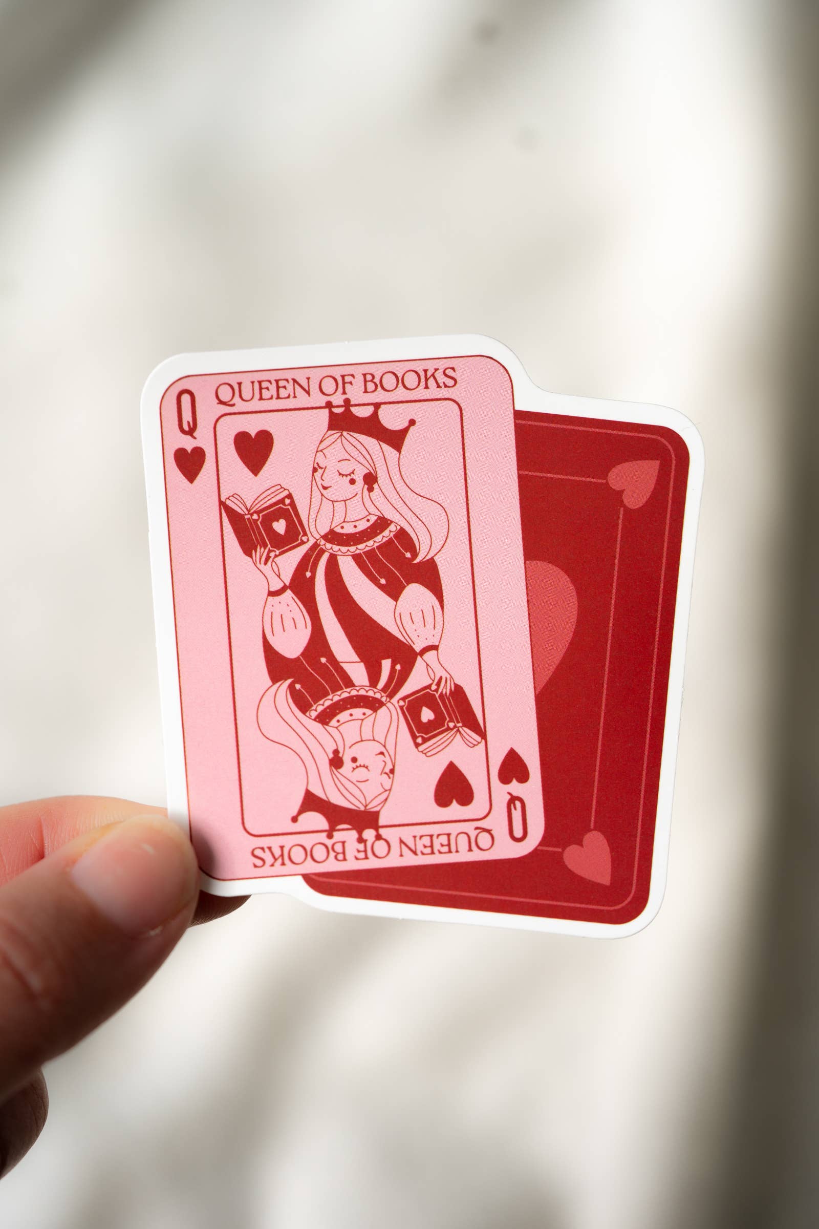 Queen of Books playing card held by a hand against a neutral background