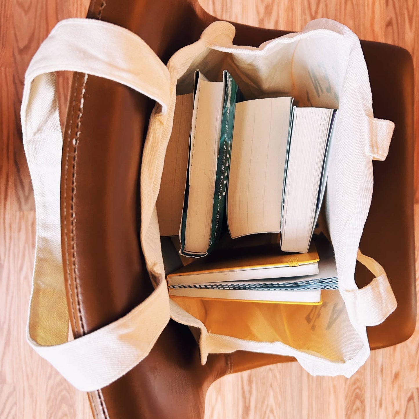 Brown leather bag with white lining containing books on a wooden surface