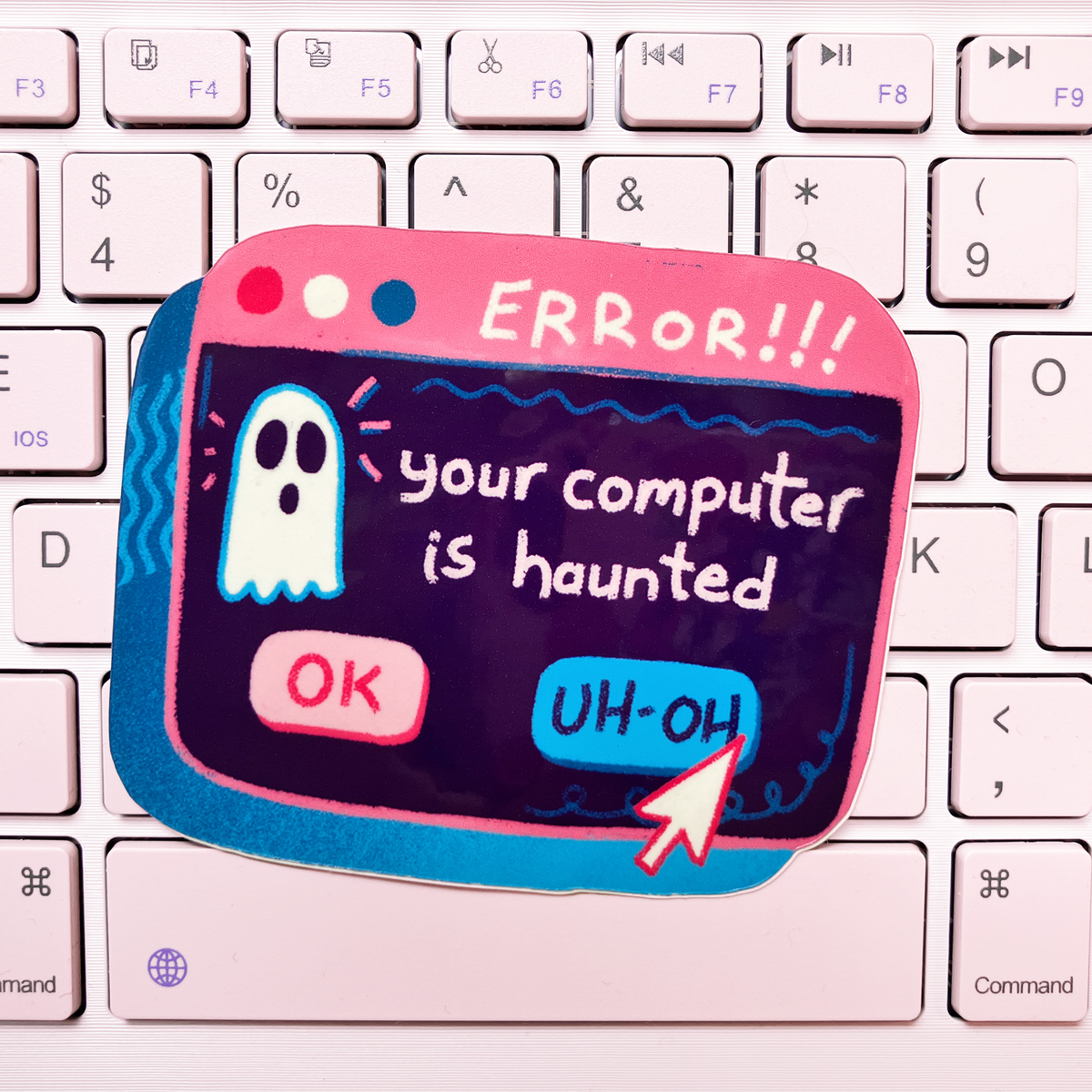 A novelty keyboard sticker shaped like a computer error window, featuring a ghost and the text 'ERROR!!! your computer is haunted' with 'OK' and 'UH-OH' buttons, placed on a white keyboard.