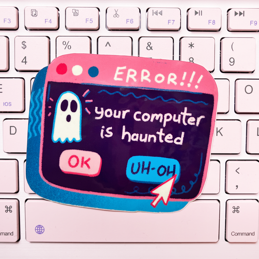 A novelty keyboard sticker shaped like a computer error window, featuring a ghost and the text 'ERROR!!! your computer is haunted' with 'OK' and 'UH-OH' buttons, placed on a white keyboard.