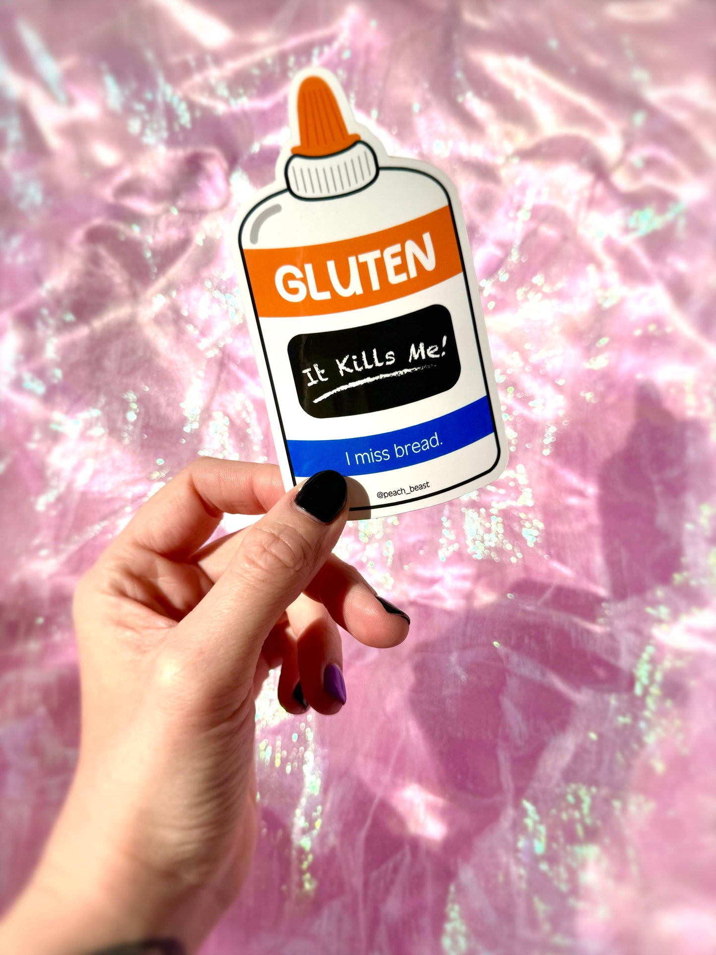 Sticker of a gluten bottle labeled 'It Kills Me! I miss bread' held by a hand against a pink glittery background.