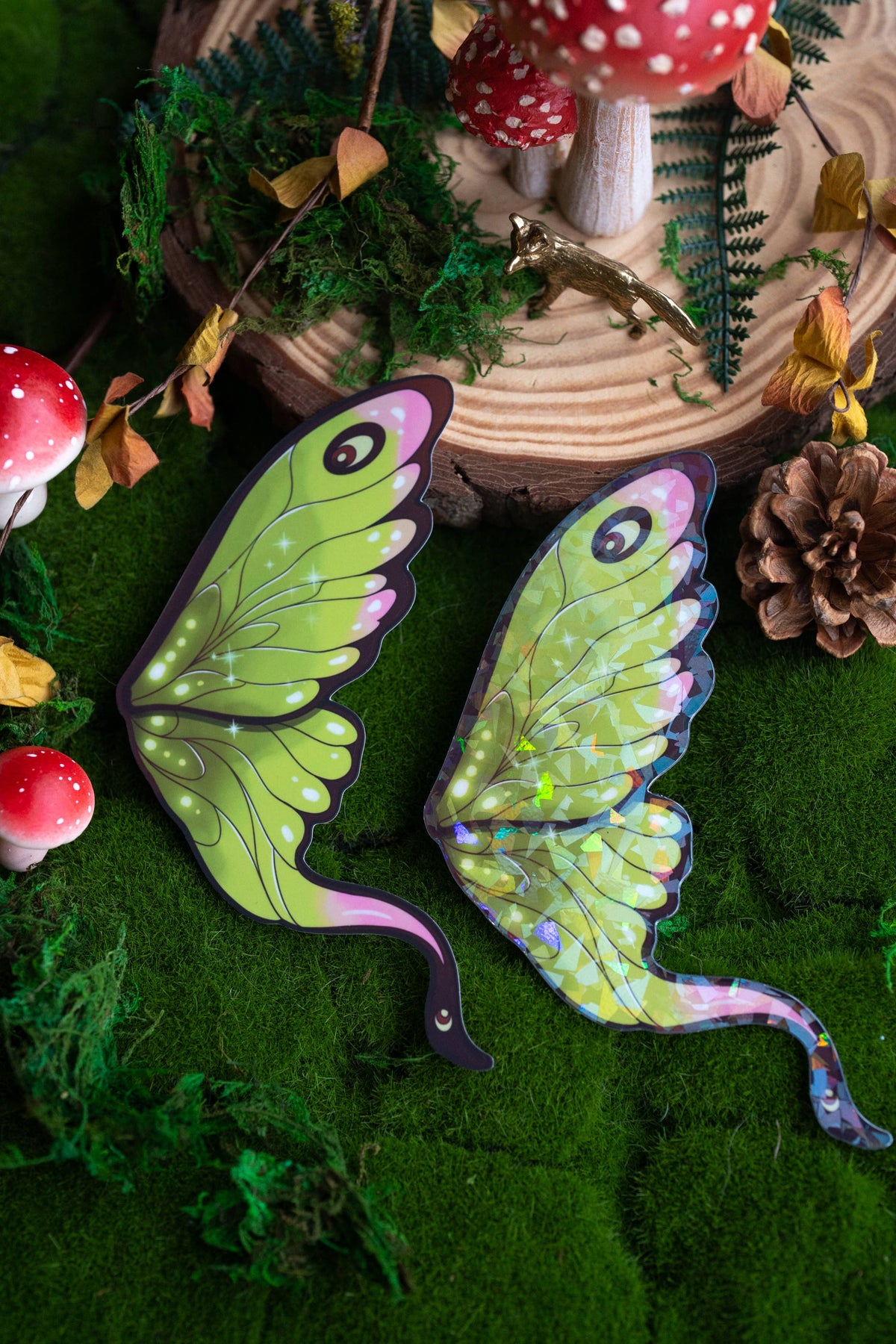 Green fairy wings with purple accents on a forest-themed background with mushrooms and pinecones.