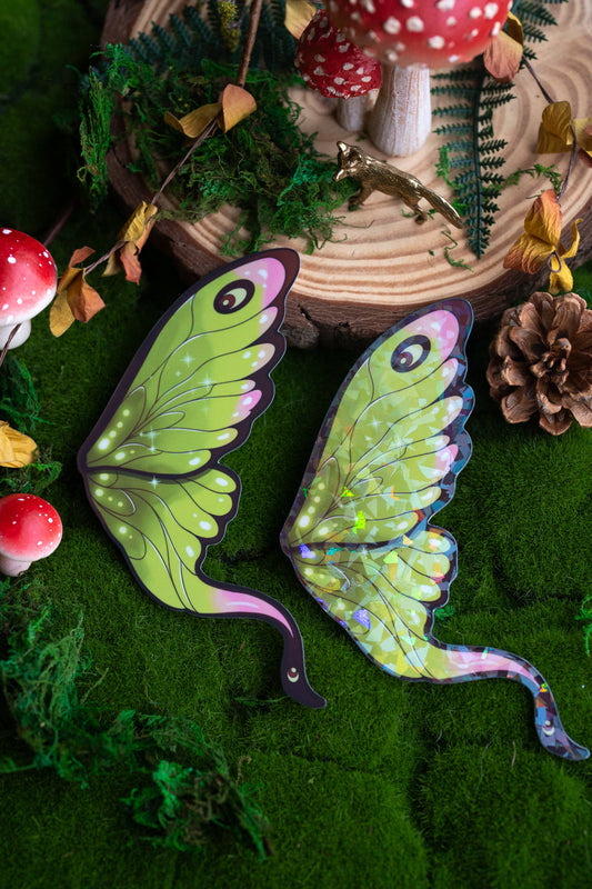 Green fairy wings with purple accents on a forest-themed background with mushrooms and pinecones.