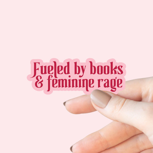 Hand holding a pink sticker with 'Fueled by books & feminine rage' text on a pink background
