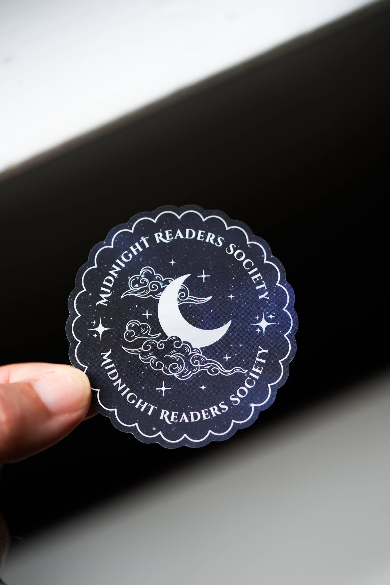 Sticker with 'Midnight Readers Society' design held over a black surface.