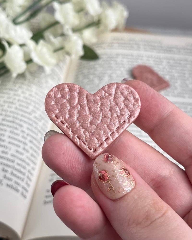 Heart-shaped pink object held by a hand with floral background