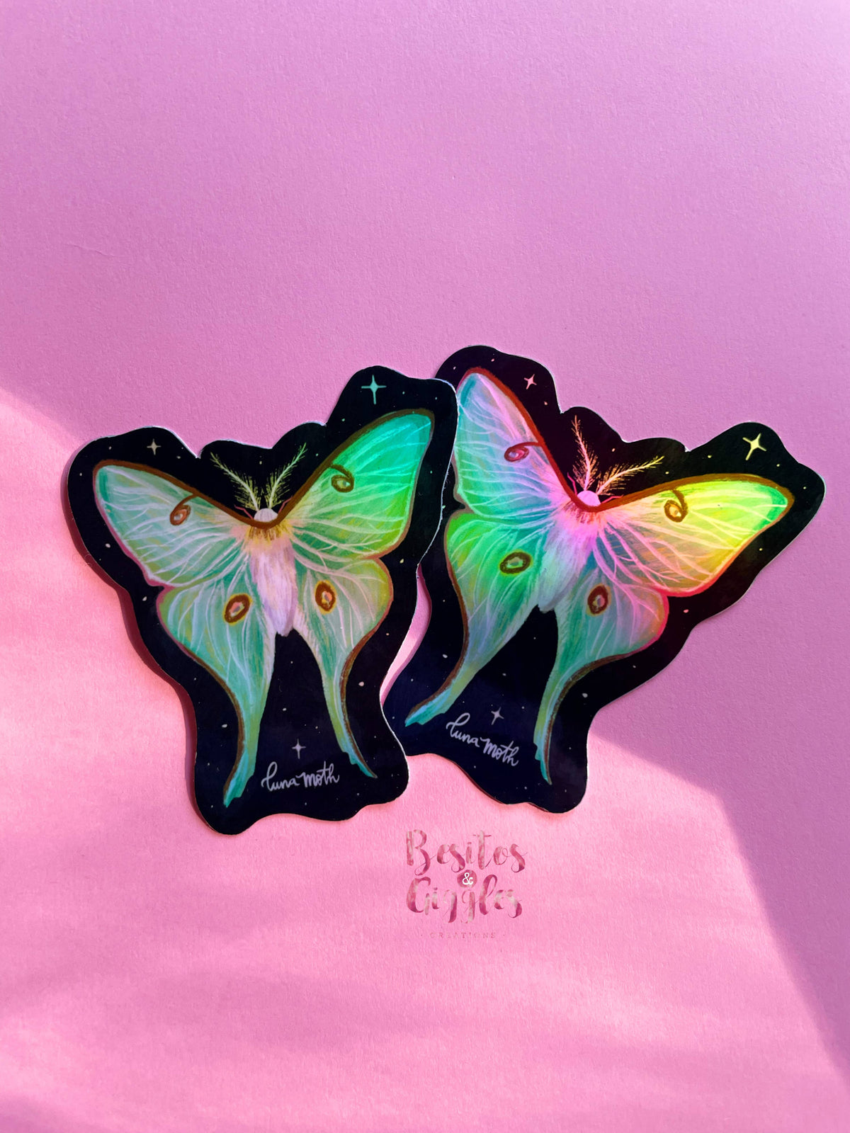 Two butterfly-shaped stickers with iridescent pastel wings on a black starry background, displayed on a pink surface with the text 'Besties Craft' below them.