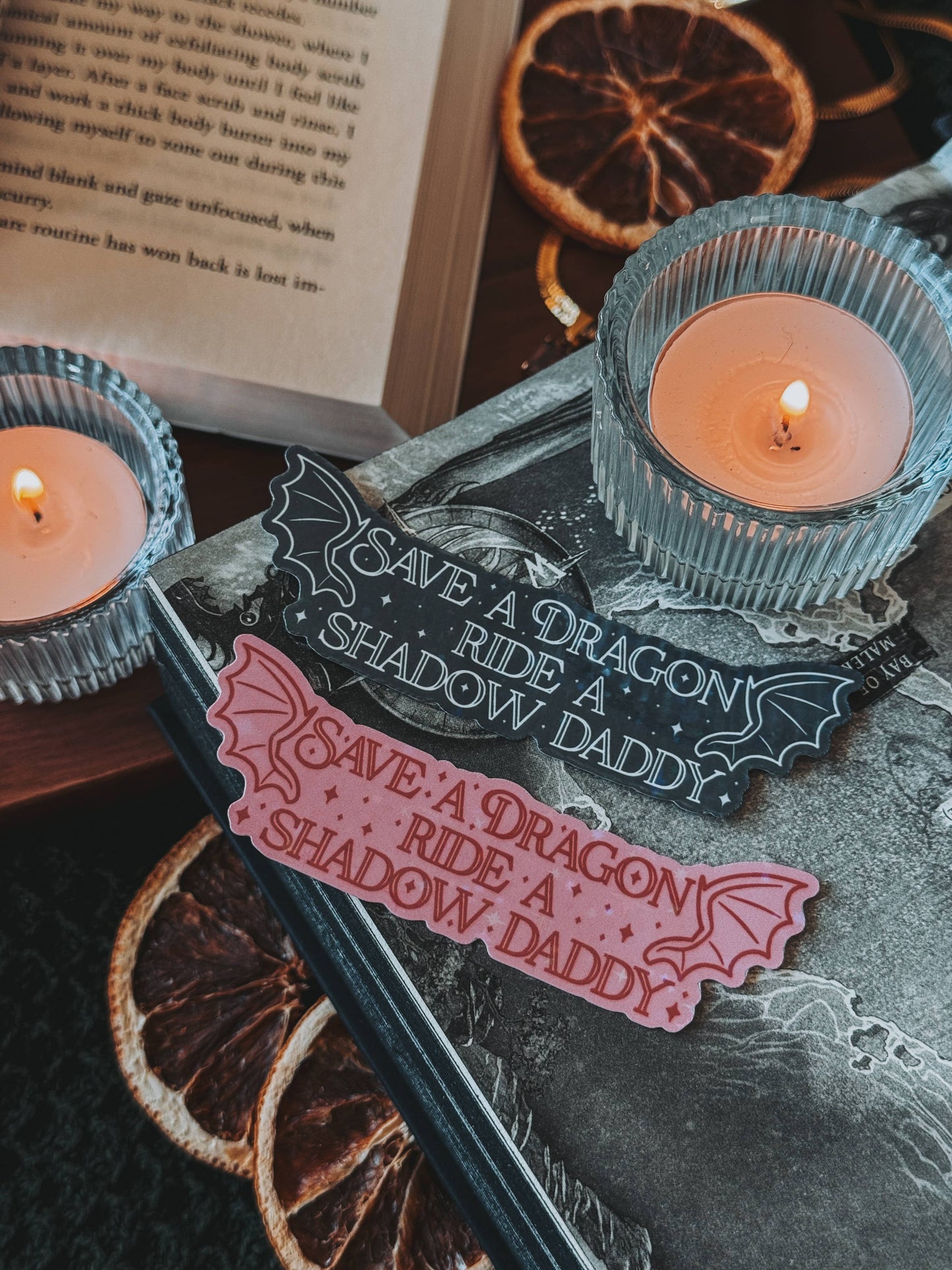 Decorative items with 'Save a Dragon, Ride a Shadow Daddy' text on a dark surface with candles.