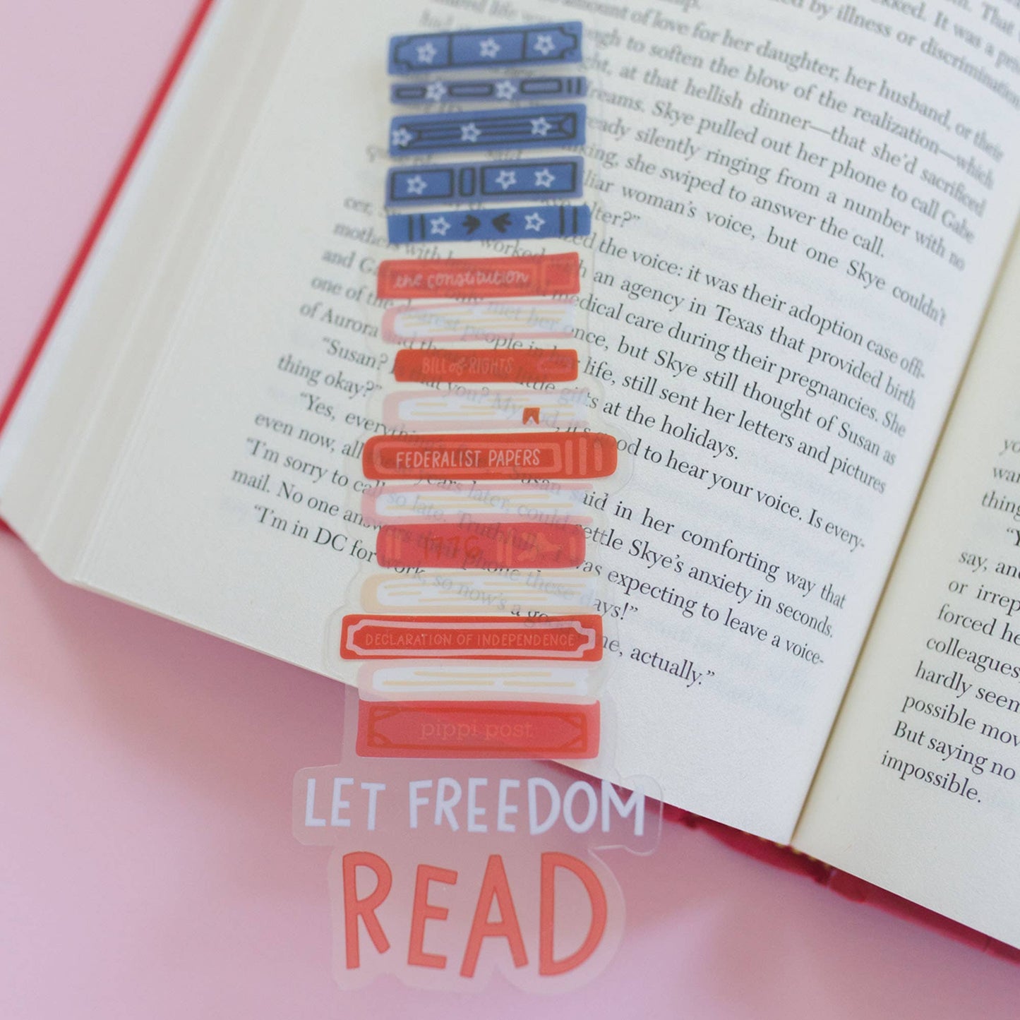 Book with a clear plastic bookmark featuring red and blue flags, on a pink surface with 'Let Freedom Read' text.