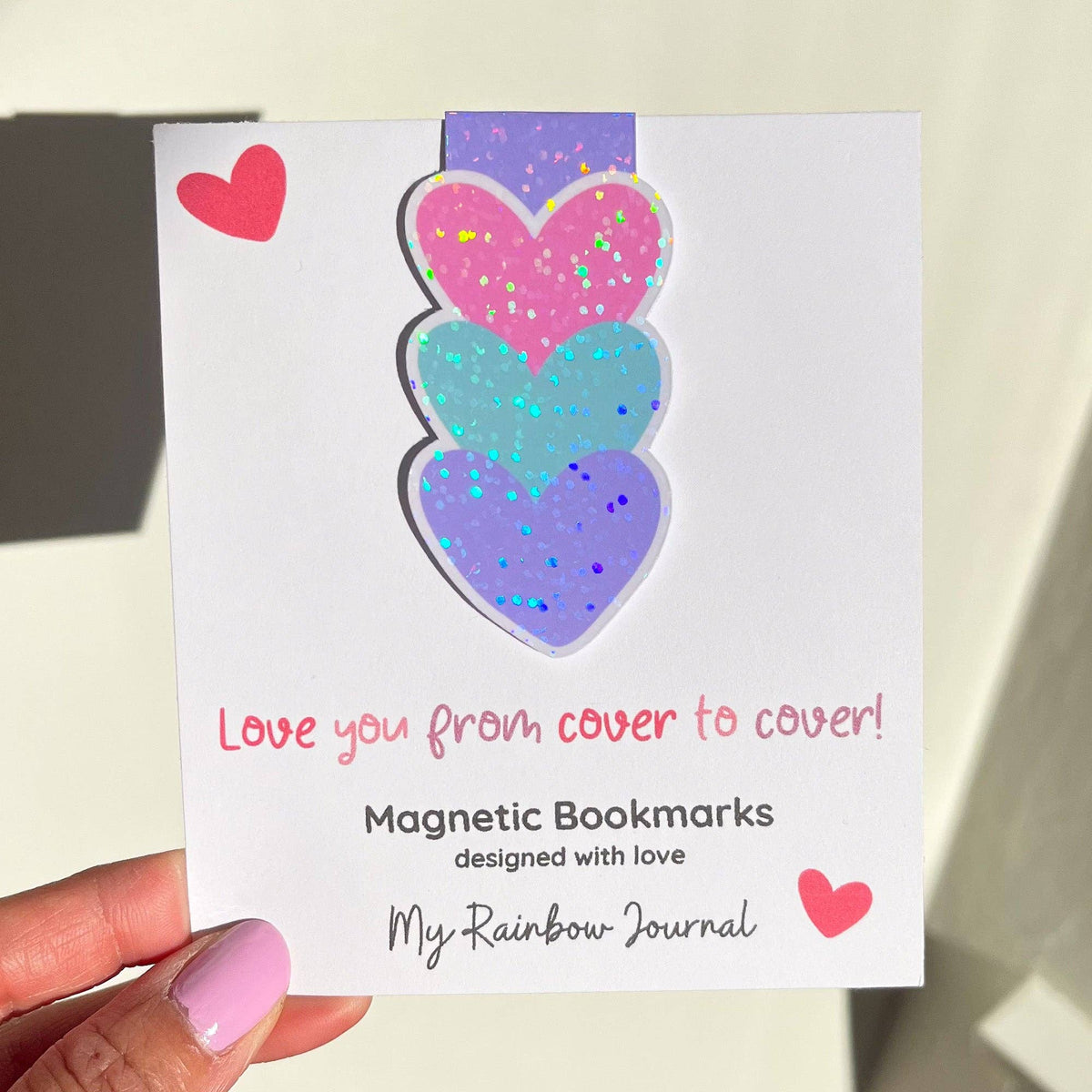 Magnetic bookmarks with heart designs on a card held by a hand.