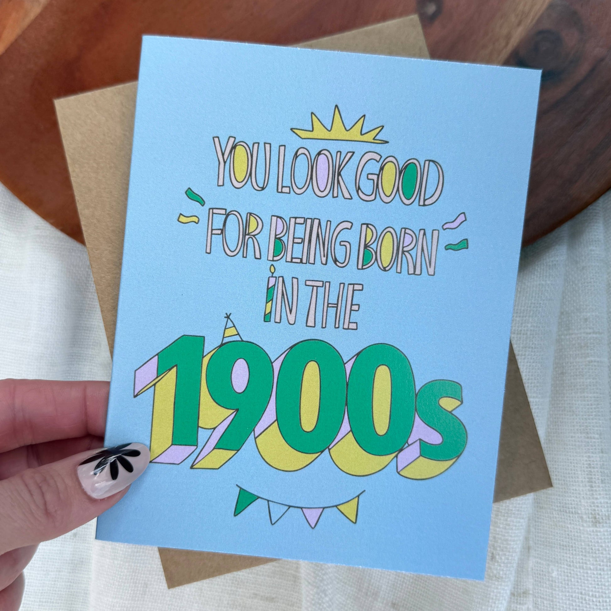 Card with humorous text 'You look good for being born in the 1900s' held by a hand.