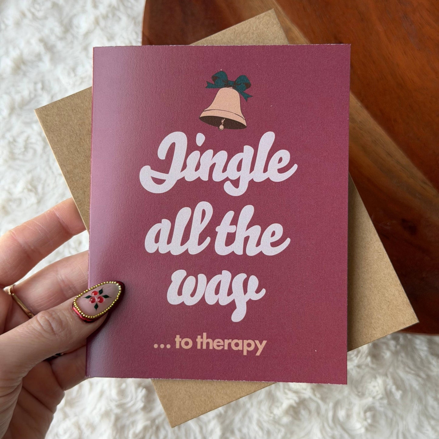 A hand holds a maroon greeting card that reads 'Jingle all the way .
