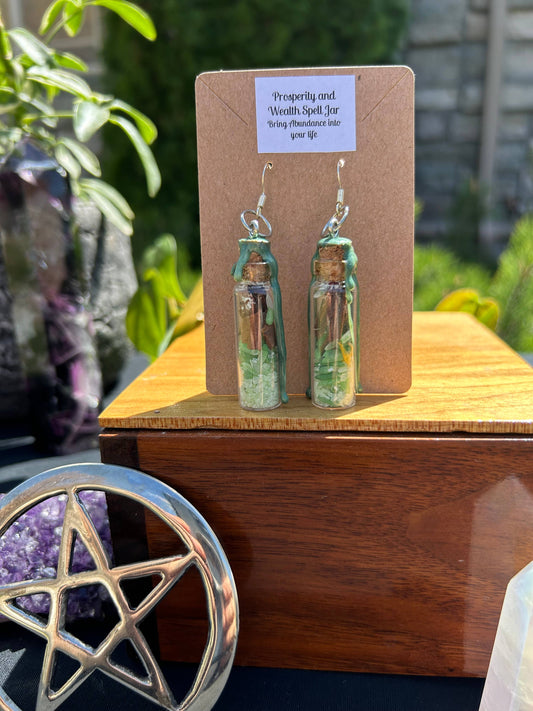 Bottle-shaped earrings on a display card with a wooden surface and plants in the background