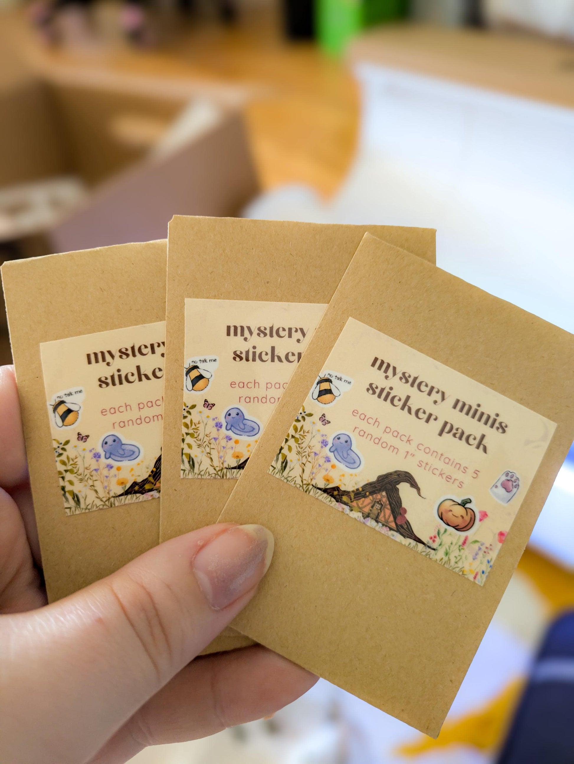 Three small brown paper packages labeled 'mystery sticker' held by a hand.