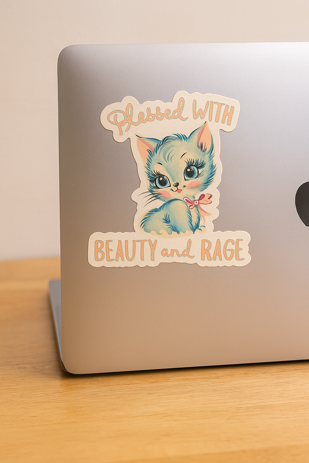 Laptop with a sticker of a cat with text 'Packed With Beauty and Rage' on a wooden surface.