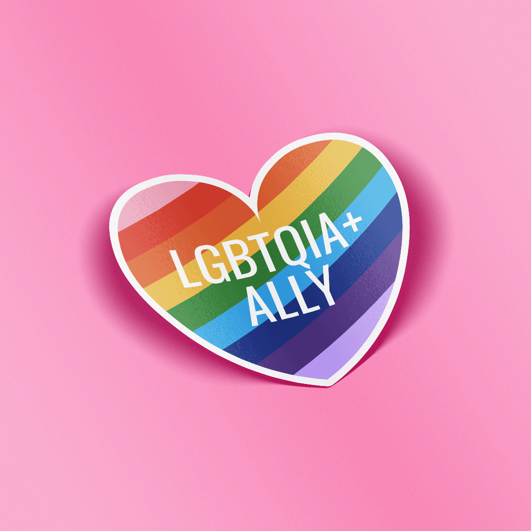 A heart-shaped sticker with a rainbow stripe pattern and the text 'LGBTQIA+ ALLY' in white, shown on a solid pink background.