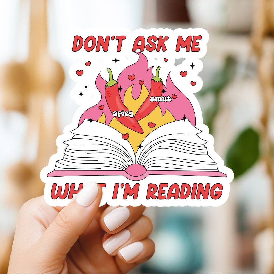 Sticker with an open book and chili peppers, held by a hand, with text 'Don't ask me what I'm reading'.