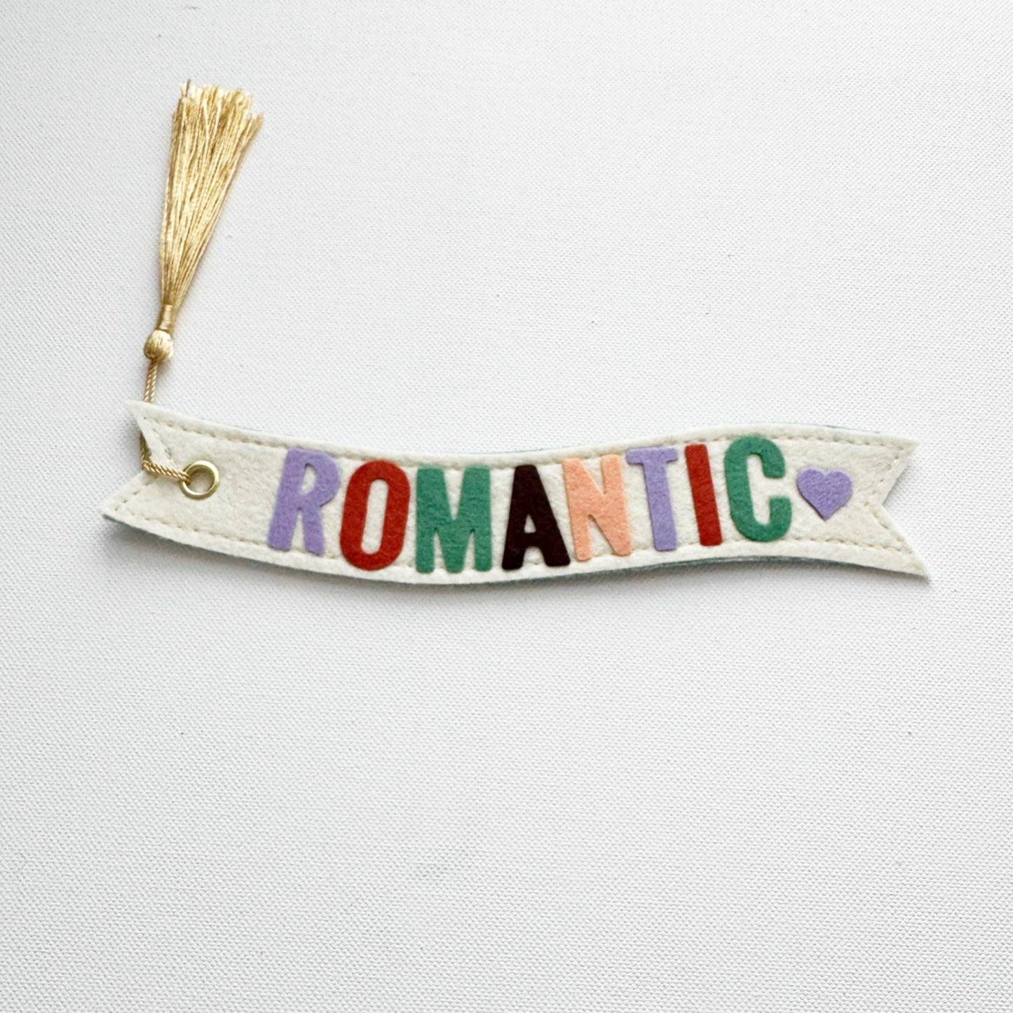 Decorative banner with 'ROMANTIC' in colorful letters and a tassel on a light gray background