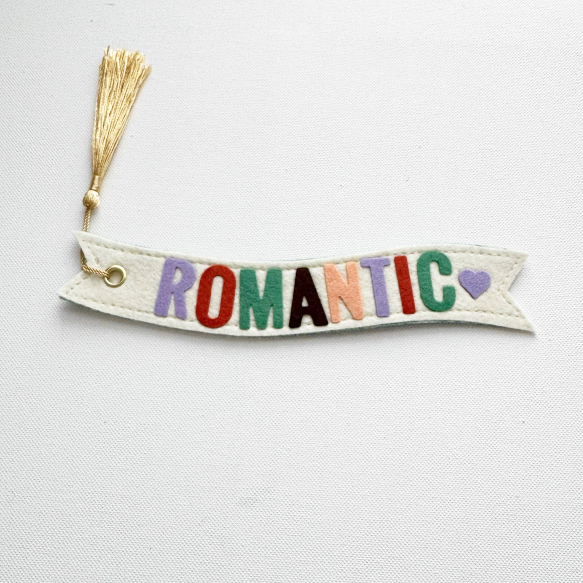 Decorative banner with 'ROMANTIC' in colorful letters and a tassel on a light gray background