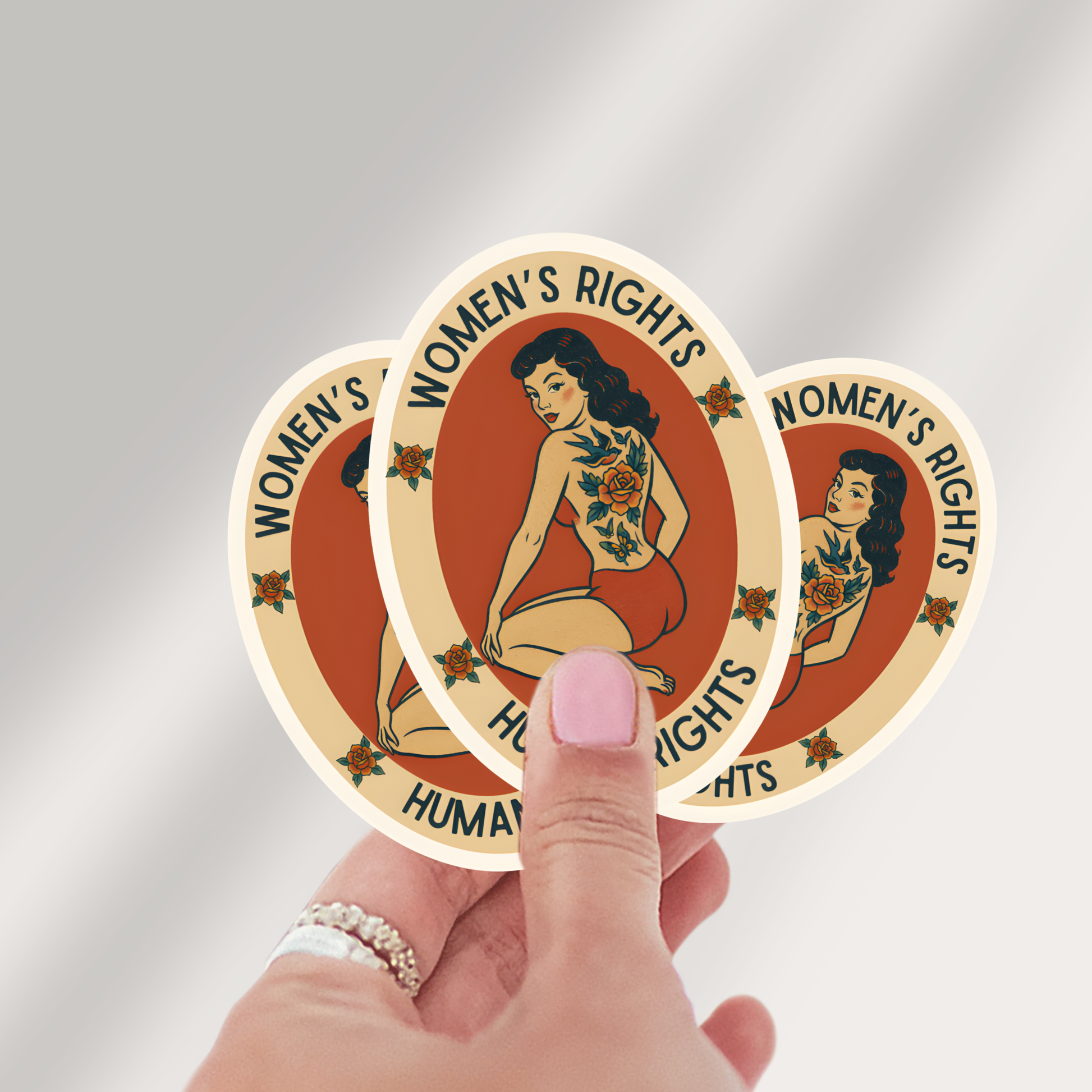 Three 'Women's Rights Human Rights' stickers held by a hand against a gray background