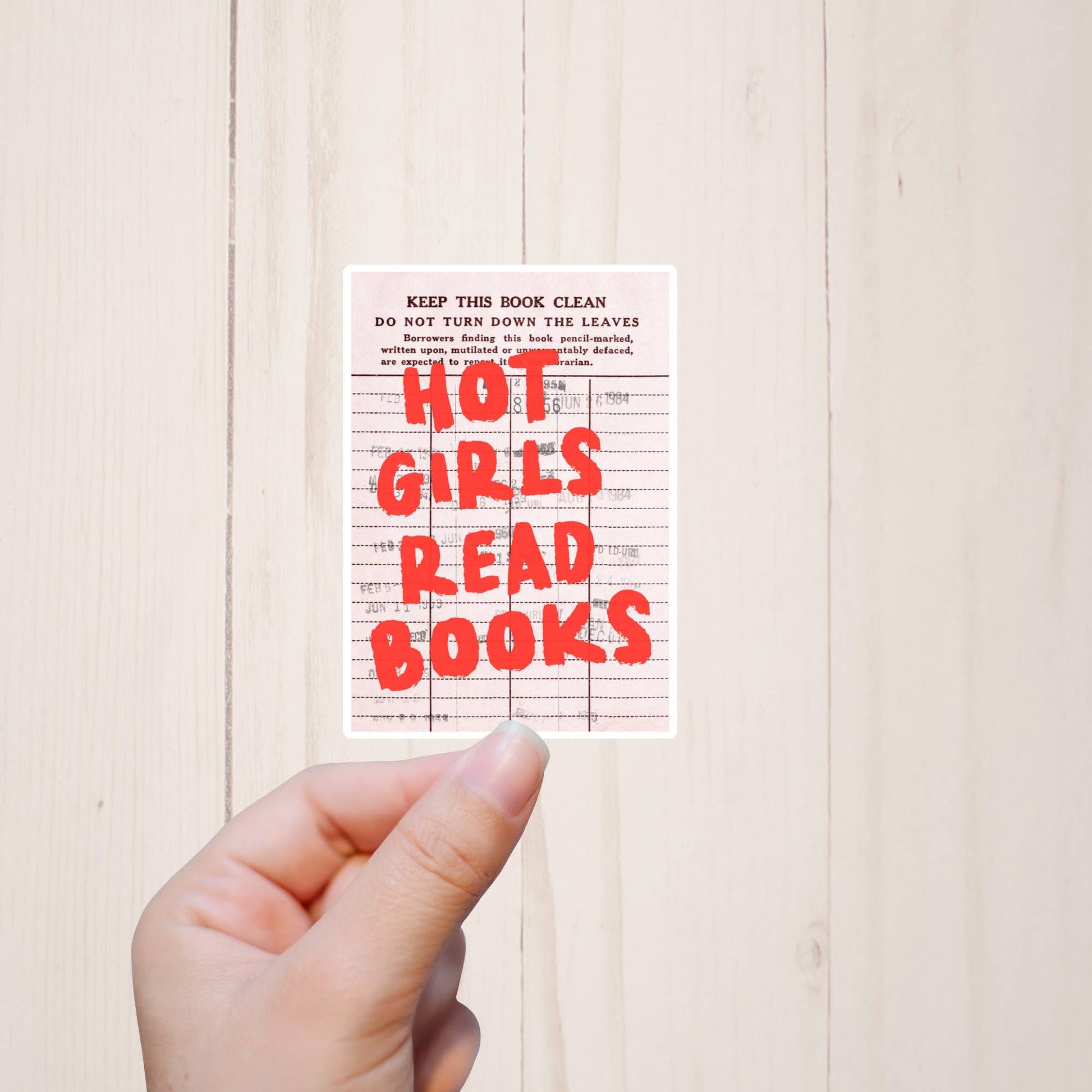Hand holding a book with 'Hot Girls Read Books' text on a light wooden background
