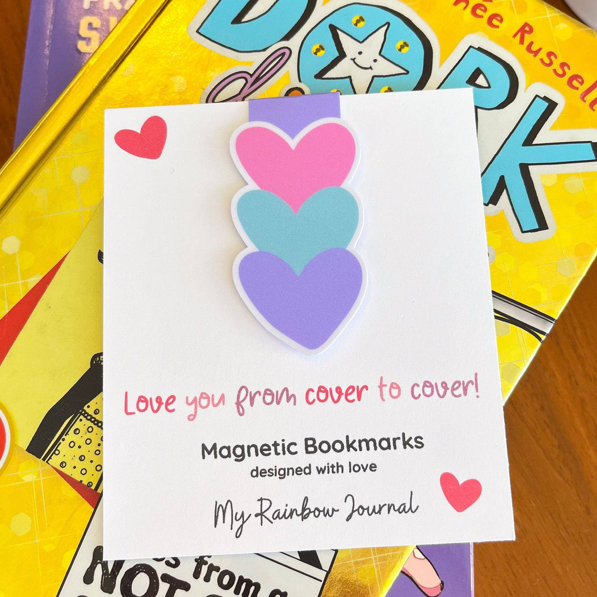 Magnetic bookmarks with heart designs on a card, placed on top of a colorful book.