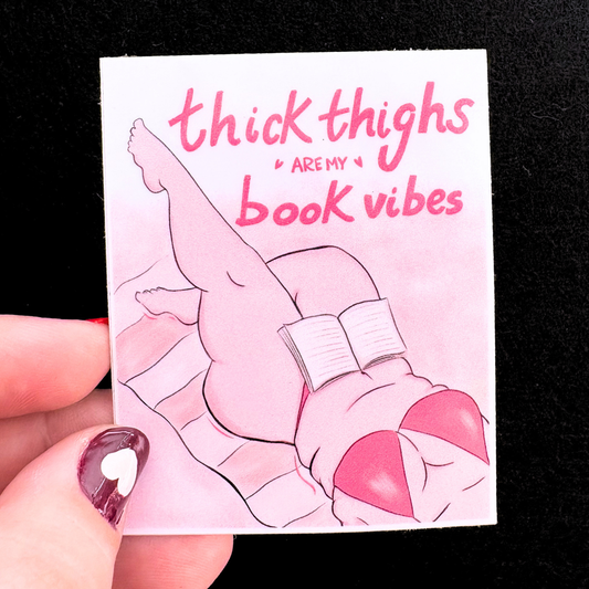 Card with illustration of legs in pink bikini holding a book, text 'thick thighs are my book vibes' on a black background.