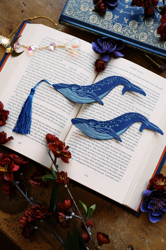 Blue whale-shaped bookmarks on an open book with flowers around