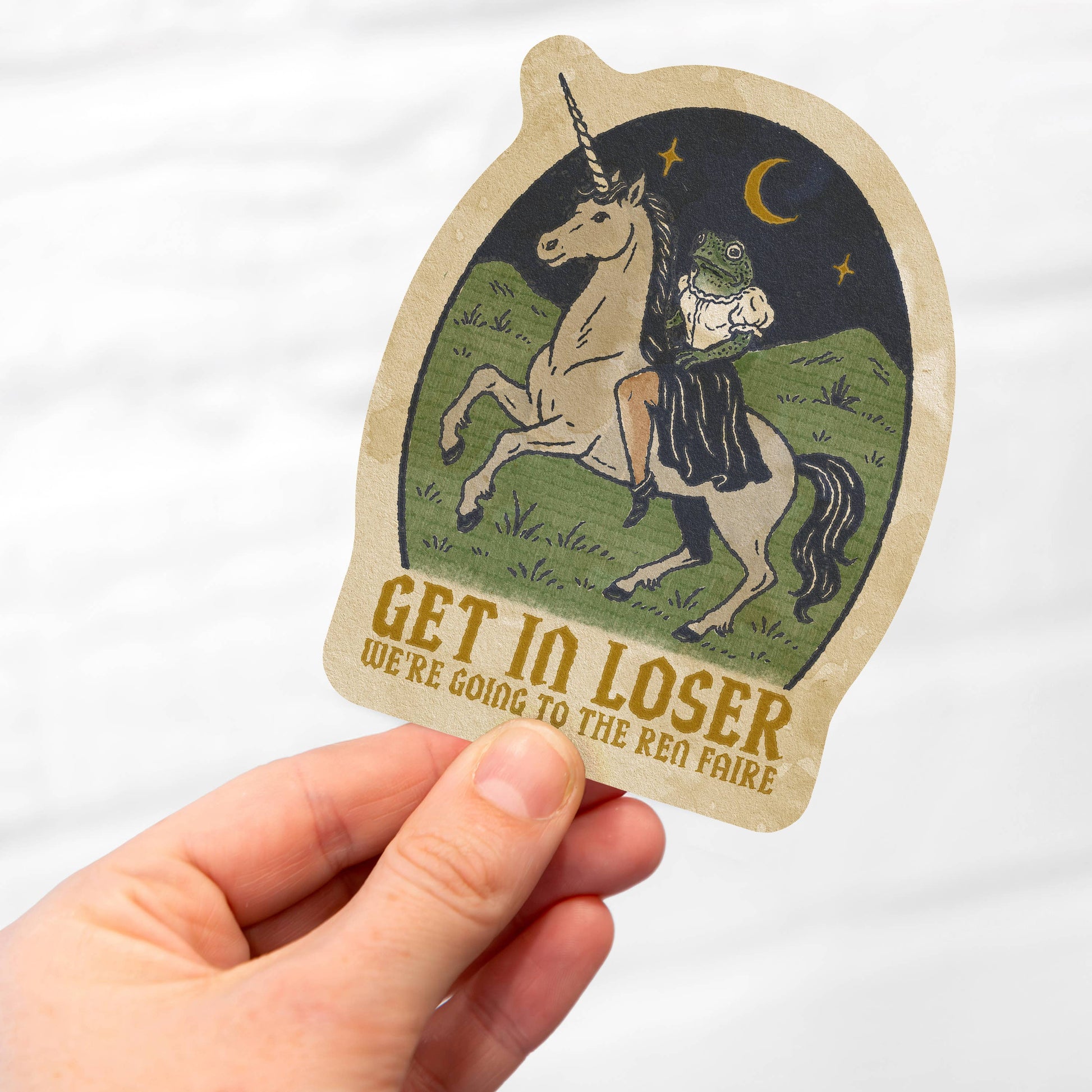 Hand holding a sticker with a unicorn and text on a white background