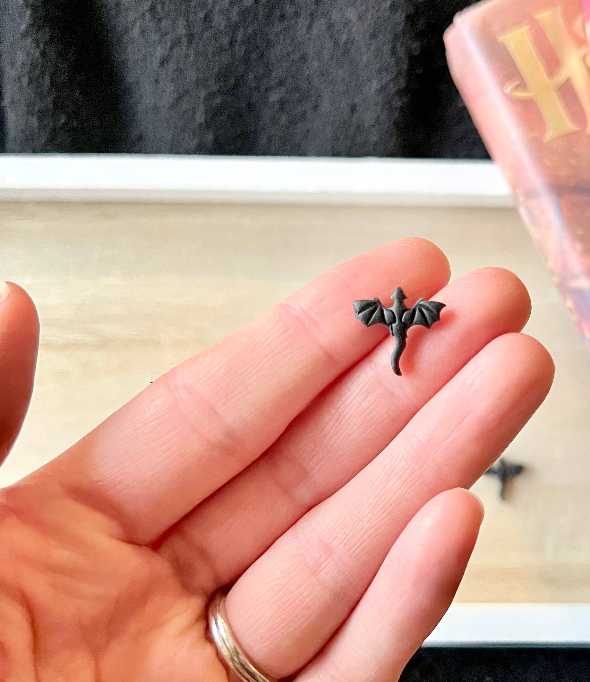 Small dragon-shaped earring held between fingers with a blurred background