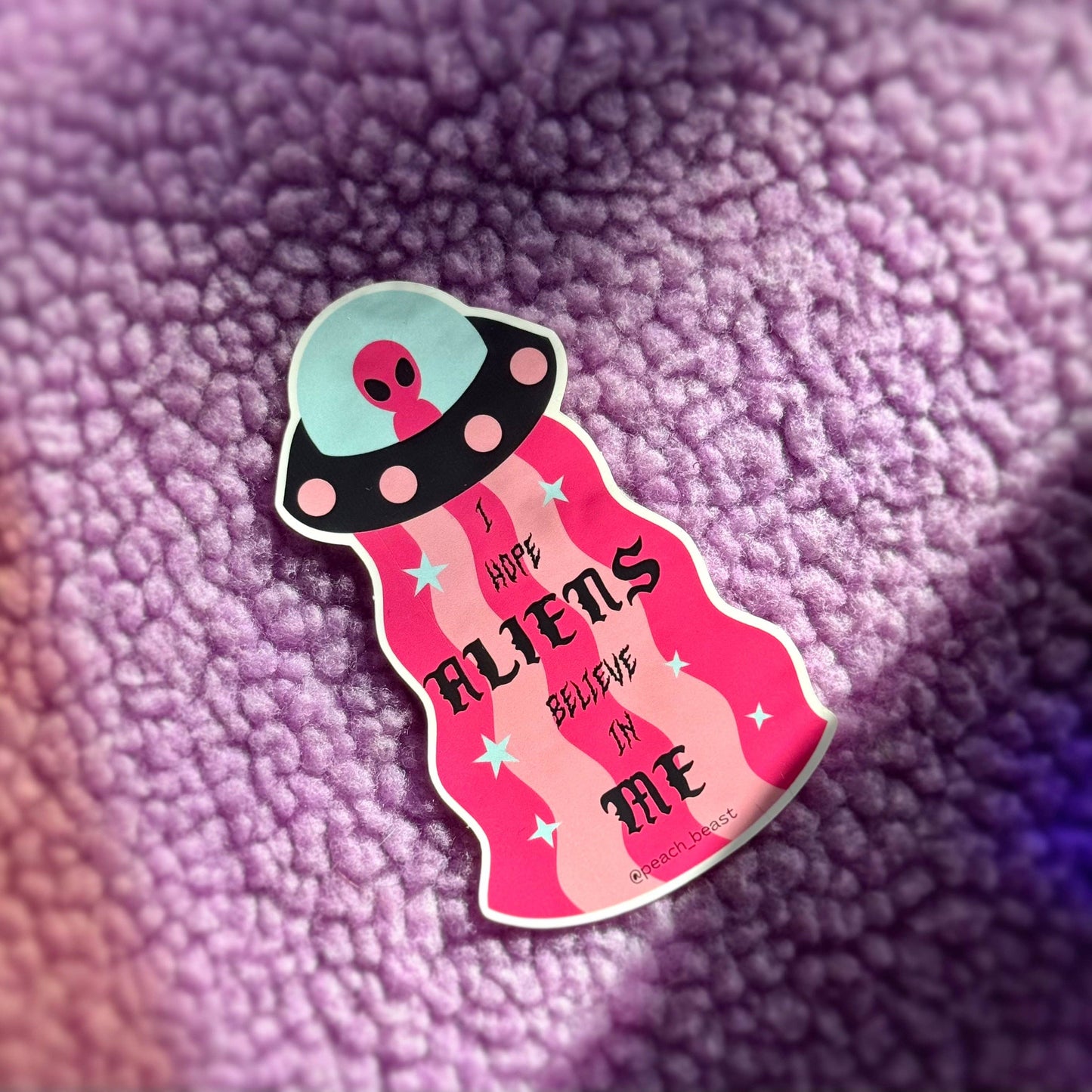 Sticker with alien design and text 'I hope aliens believe in me' on a textured purple background
