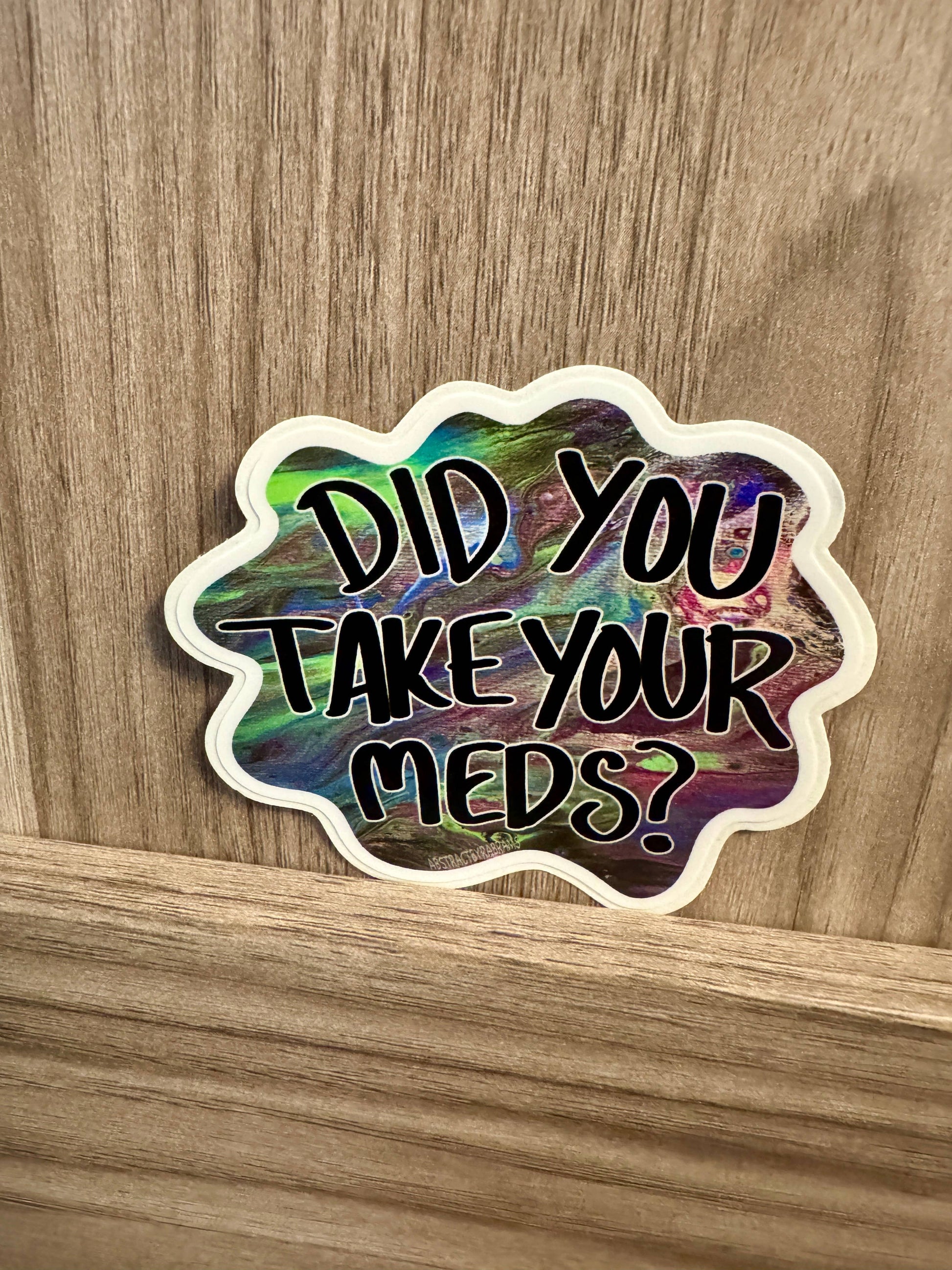 Holographic sticker with text 'Did you take your meds?' on a wooden surface
