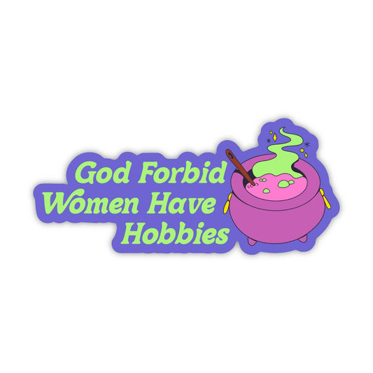 A die-cut sticker featuring the text 'God Forbid Women Have Hobbies' in light green bubble letters on a purple background, next to an illustration of a pink cauldron with green potion and a wooden spoon, all on a plain white background.