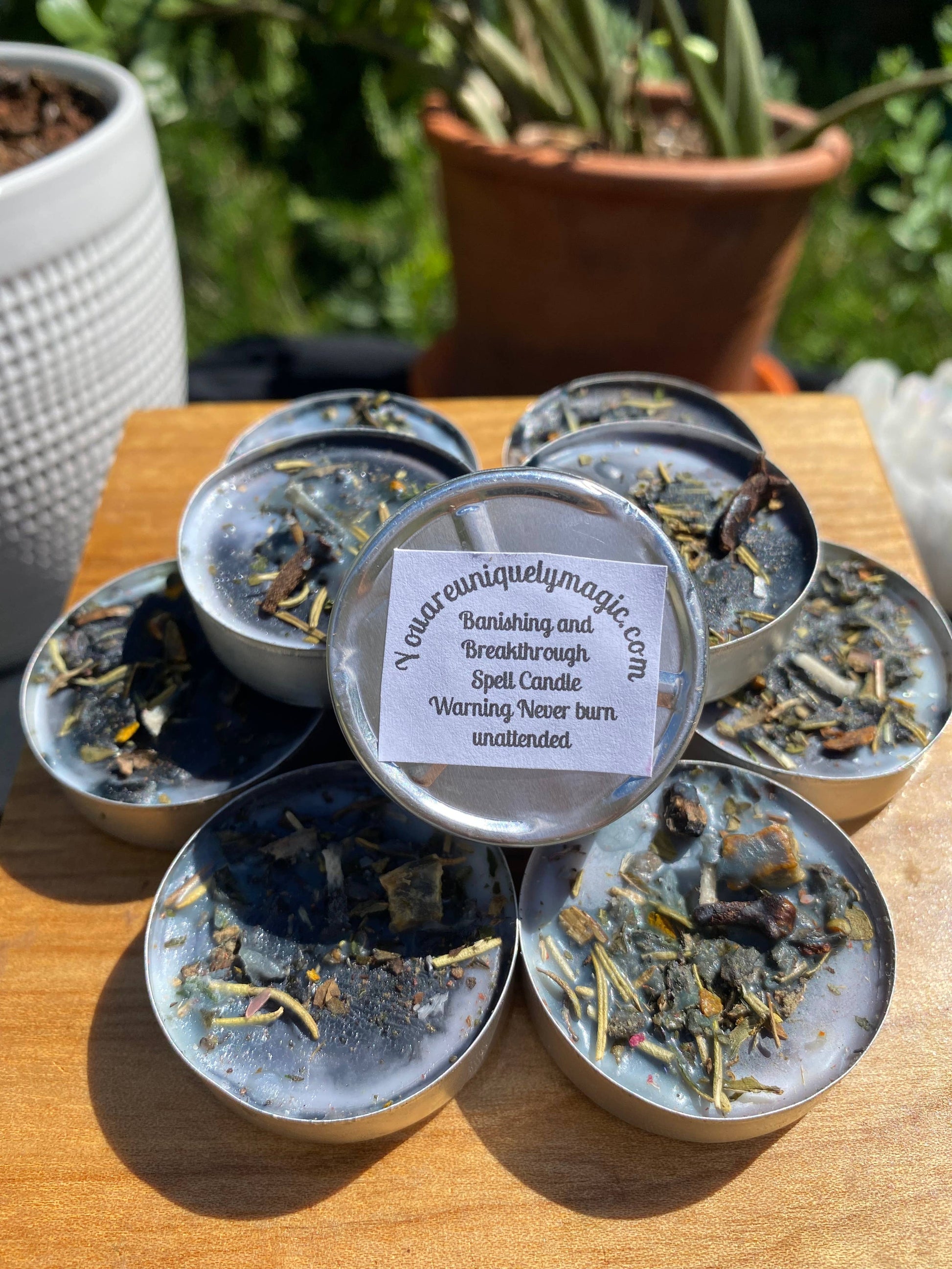 Collection of small candles in tins on a wooden surface with plants in the background.