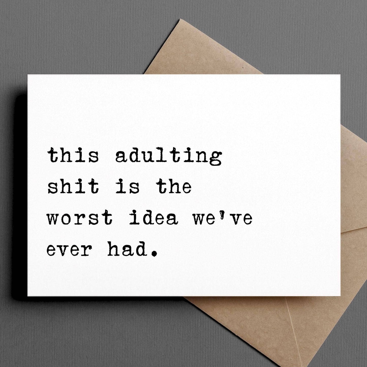 Card with humorous text 'this adulting shit is the worst idea we've ever had' on a gray background