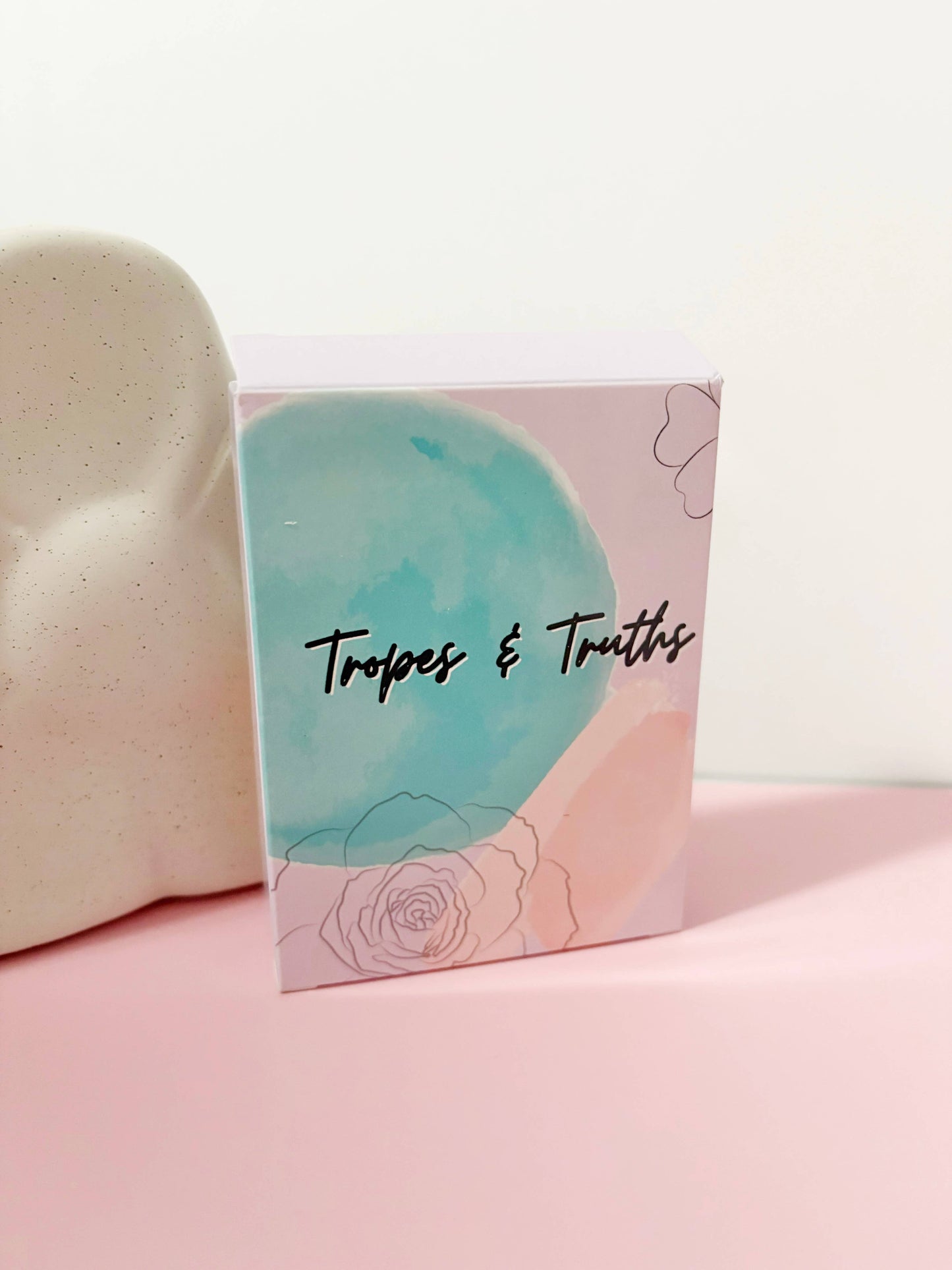 Card with 'Tropes & Truths' text on a pink and blue design, placed on a pink surface.