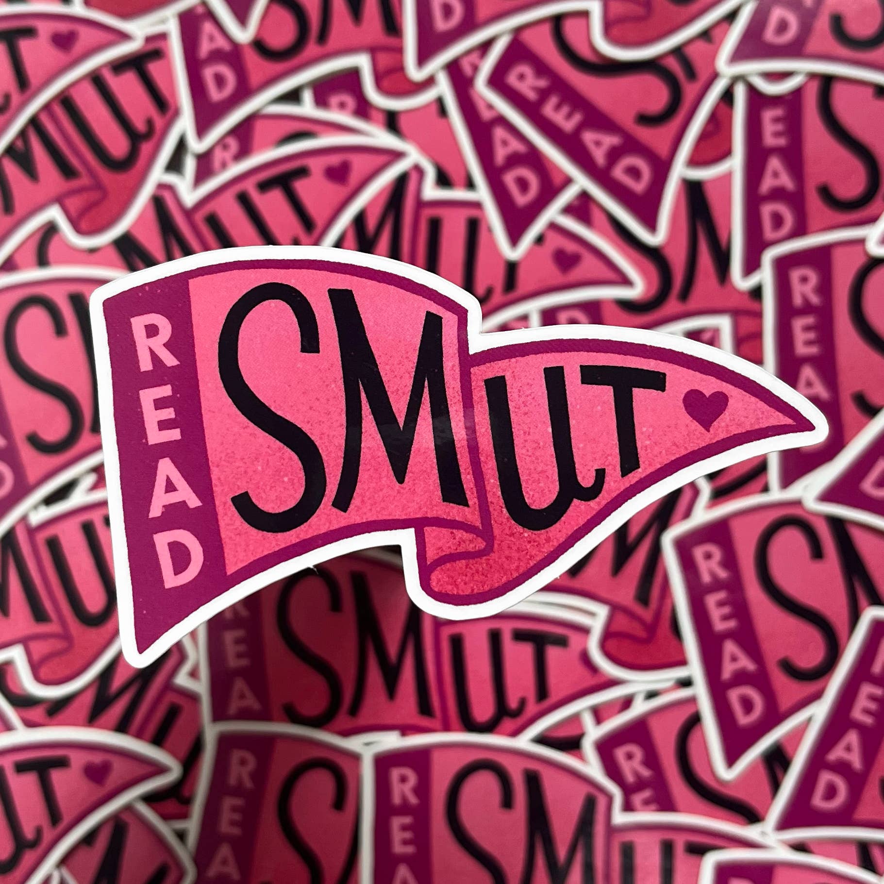 A close-up pile of die-cut stickers featuring the phrase 'READ SMUT' in black text on a pink and magenta banner shape with a white outline.