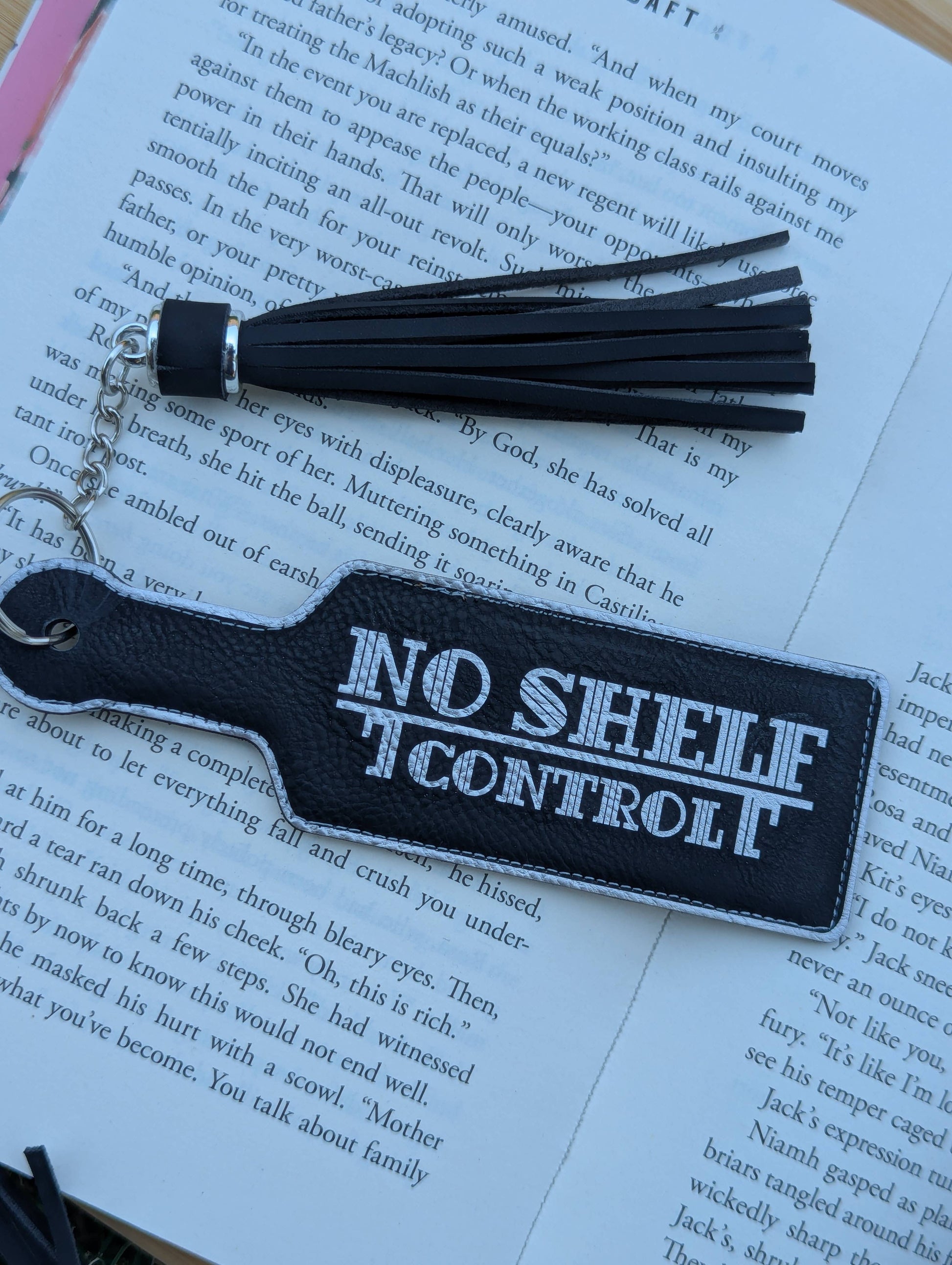 Black keychain with 'No Shelf Control' text on an open book