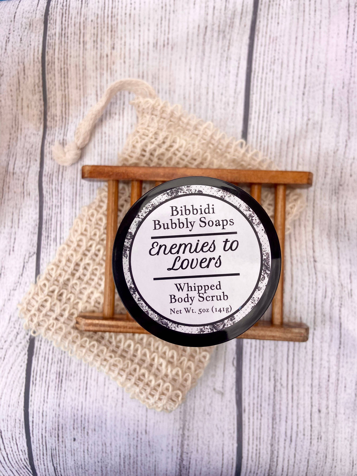 Bibbidi Bubbly Soaps whipped body scrub with a loofah on a wooden stand.