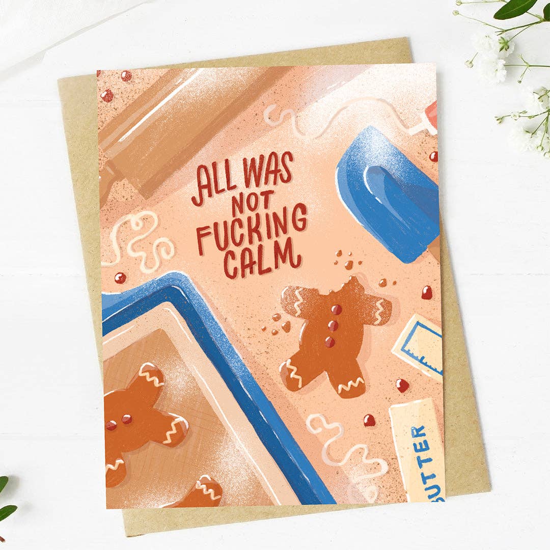 A square greeting card with a gingerbread-themed illustration and the text 'ALL WAS NOT FUCKING CALM,' shown on top of a kraft envelope on a white surface with small greenery in the corners.
